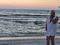 A pellican skimming the water and Janeanne standing on the beach.